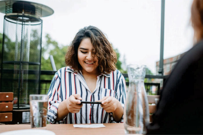 Woman using her phone to deposit a check while sitting at a table at a restaurant